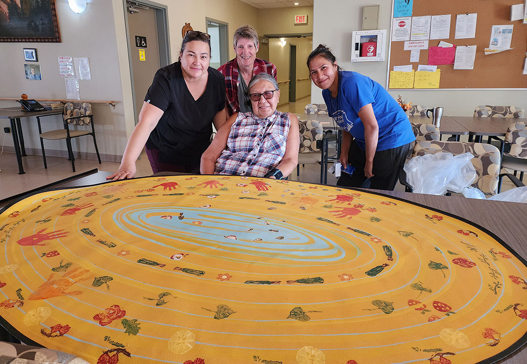 Elder Georgina Martin (seated), Margaret McGregor, Margruite Krahn, and Renee Seymour with Dankboa (in an unfinished state) which will be on display at the DCC for the duration of Resurfacing: Mennonite Floor Patterns. (Photo: Submitted)