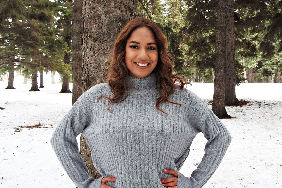 Sasha Merasty poses amidst a winter setting with trees.