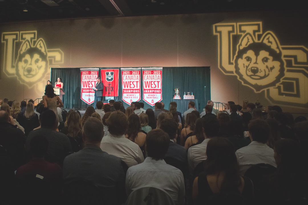 Image of Awards show with Huskie Athletics logos being projected on the wall on either side of the stage. 
