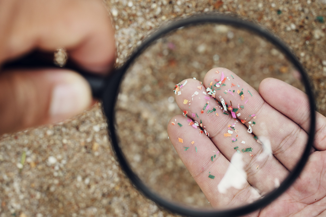 A hand holding a magnifying glass, looking at microplastics.