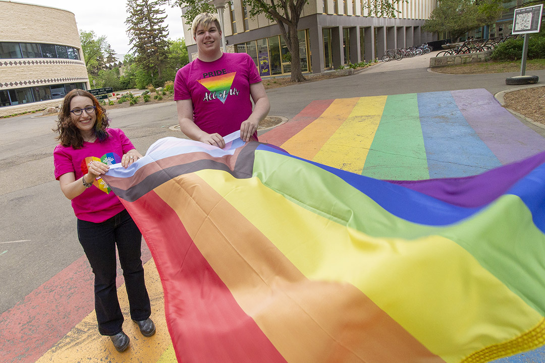 Dr. Simonne Horwitz (PhD) and USSU vice-president Jory McKay (right) hold the inclusive Pride flag, prior to being raised outside of the Peter MacKinnon Building in June of 2019. (Photo: Chris Putnam) 