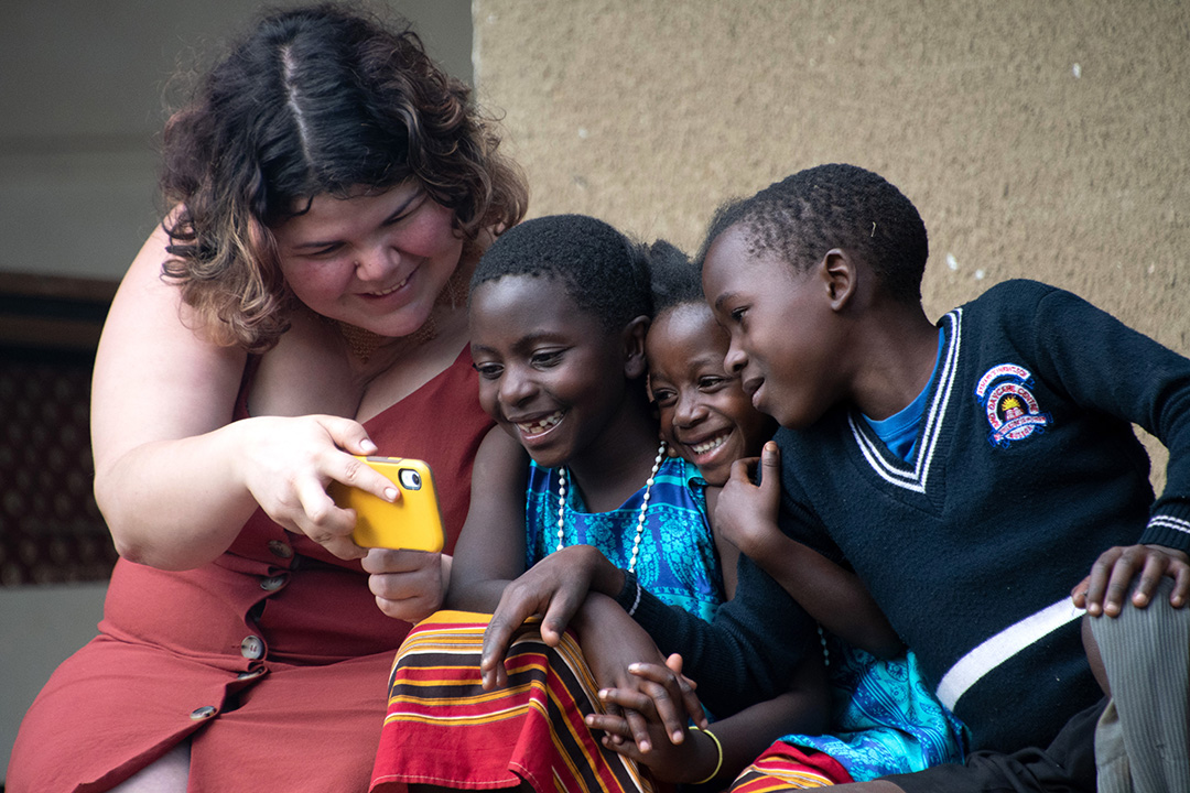 USask master’s student Zoey Roy shows kids from Uganda photos of themselves on her phone, during last spring’s Queen Elizabeth II Diamond Jubilee Scholarships program field school. (Photo: Irena Creed)