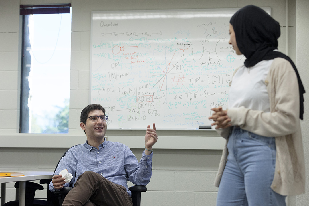 A student writes math equations on a white board in a classroom.