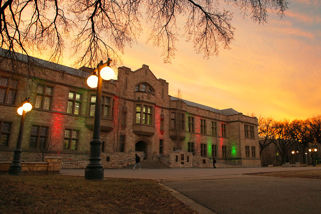 The Peter MacKinnon Building on the USask Saskatoon campus, with red and green lights and the sunrise in the background.