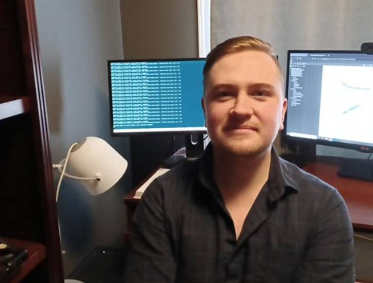 Josh Neudorf, PhD, posing for a photo in front of his computer desktop while conducting research (Photo: Submitted)