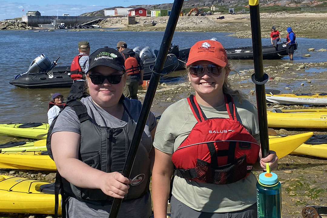 Kira Mudrey (left) and her classmate Halle Kutney (right) prepare to kayak with beluga whales in Churchill, Manitoba. The Hudson Bay can be seen in the background. 