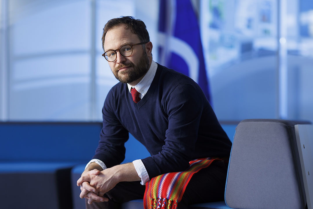 Dr. Kurtis Boyer sits in an office with a blue background, and a Métis flag in the background