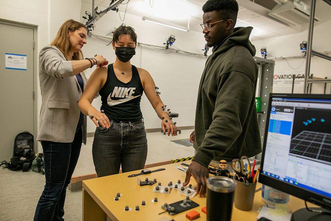 Dr. Angelica Lang (left) places a motion capture sensor on student Lauryn Campbell with the help of student Davidson Fadare. (Photo: Christina Weese)