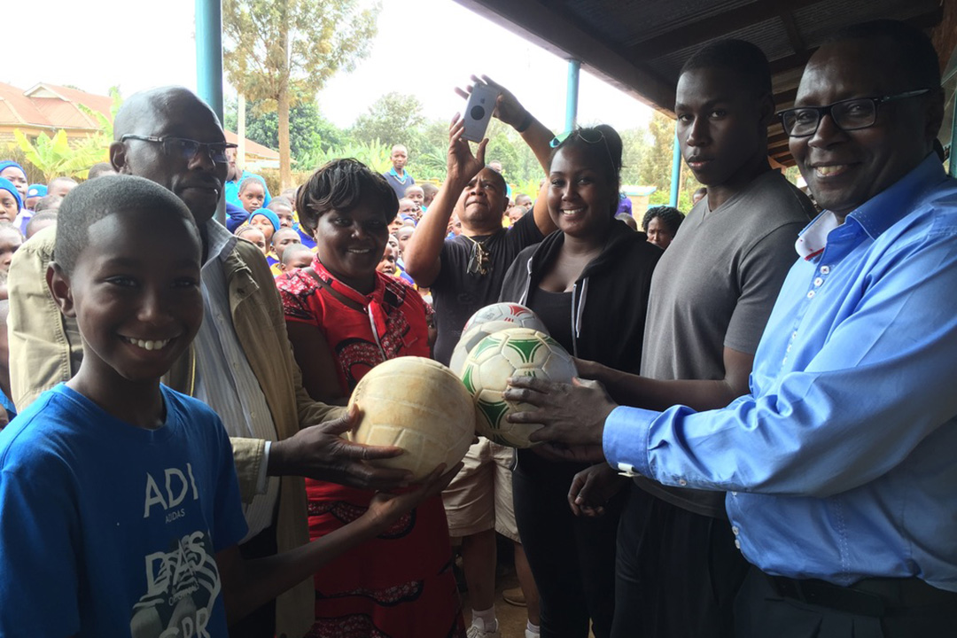 From right, Dr. George Mutwiri (DVM, PhD) and his children George Jr. and Vanessa, as well as Gitonga (at left) present soccer balls to George’s old school in Nkabune Village in Kenya in 2016. 