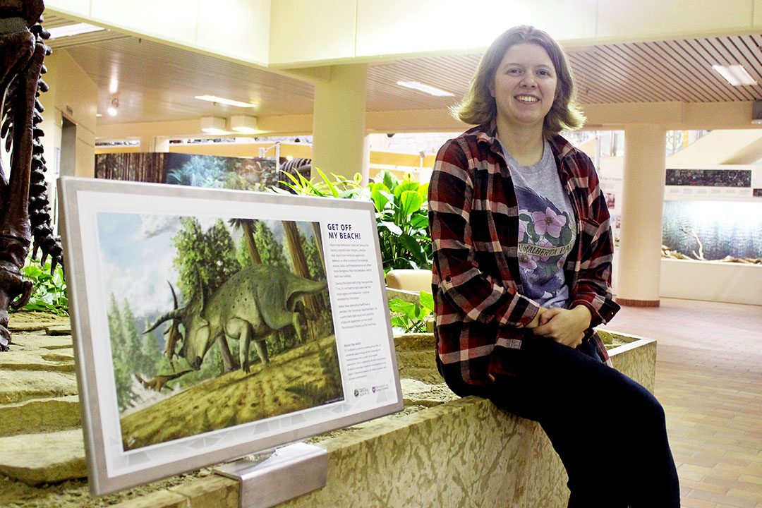 USask student Kaitlin “KT” Lindblad sits next to her paleoartistic rendition of the Triceratops in the Geology Building. (Photo by Kristen McEwen)