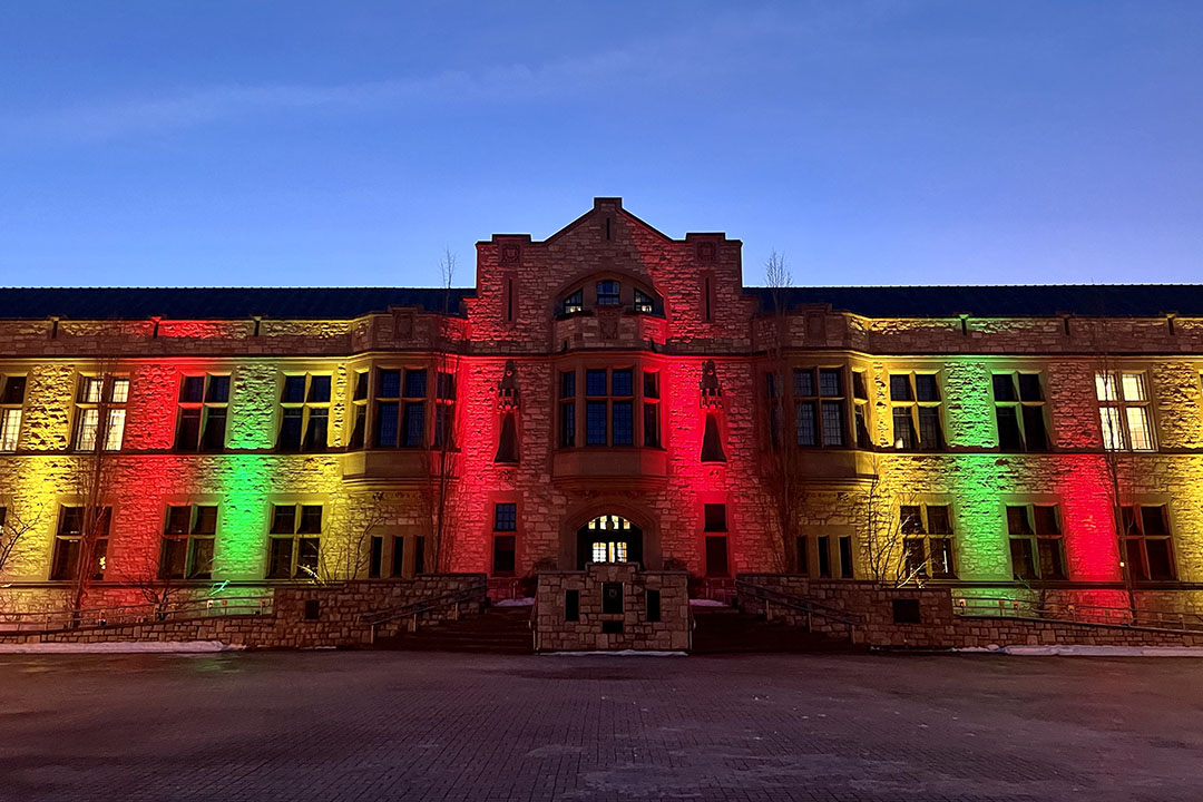 The Peter McKinnon Building at the Saskatoon University of Saskatchewan campus, with red, green, yellow spotlights to highlight Black History Month and the legacy and contributions of members of the university’s Black community.