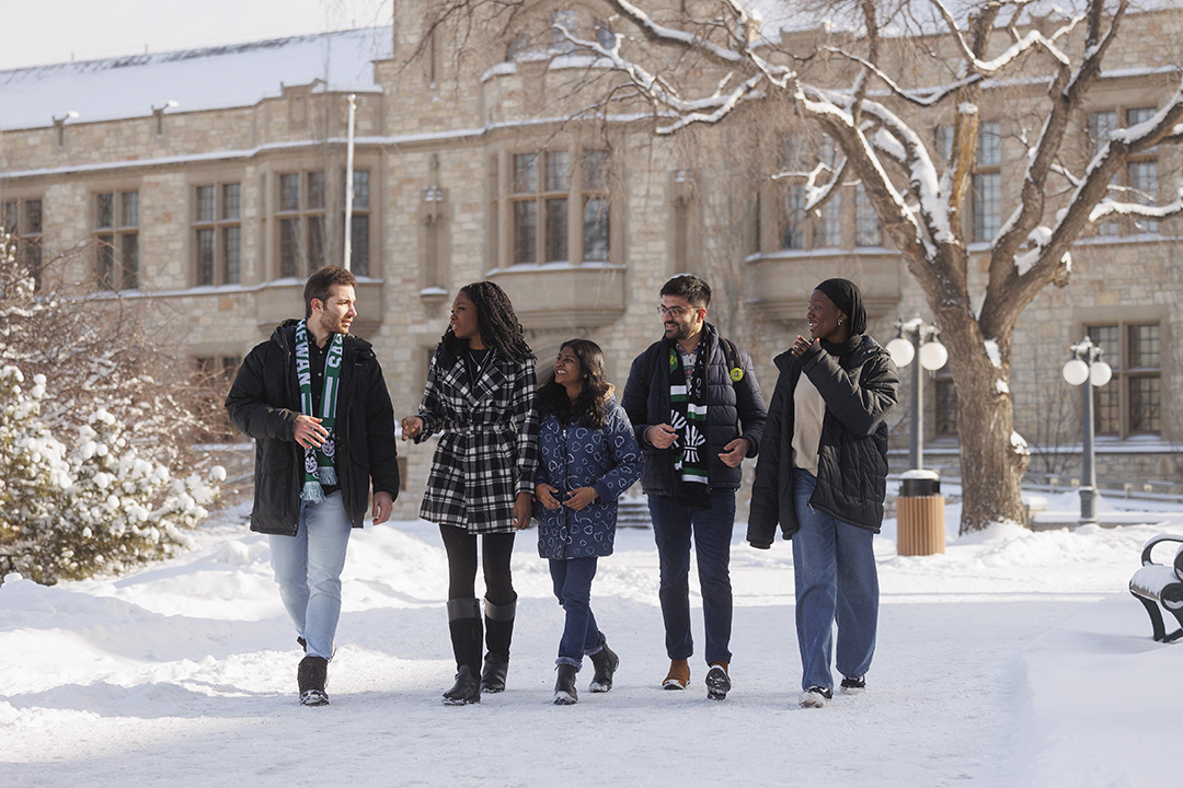 People are seen walking next to a historic building at the University of Saskatchewan during winter time.