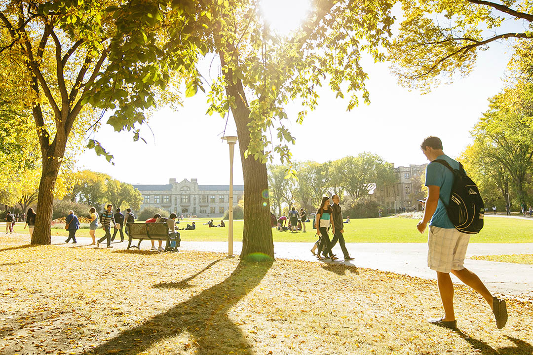 A sunny scene on campus with students walking through campus grounds with historical buildings in the background