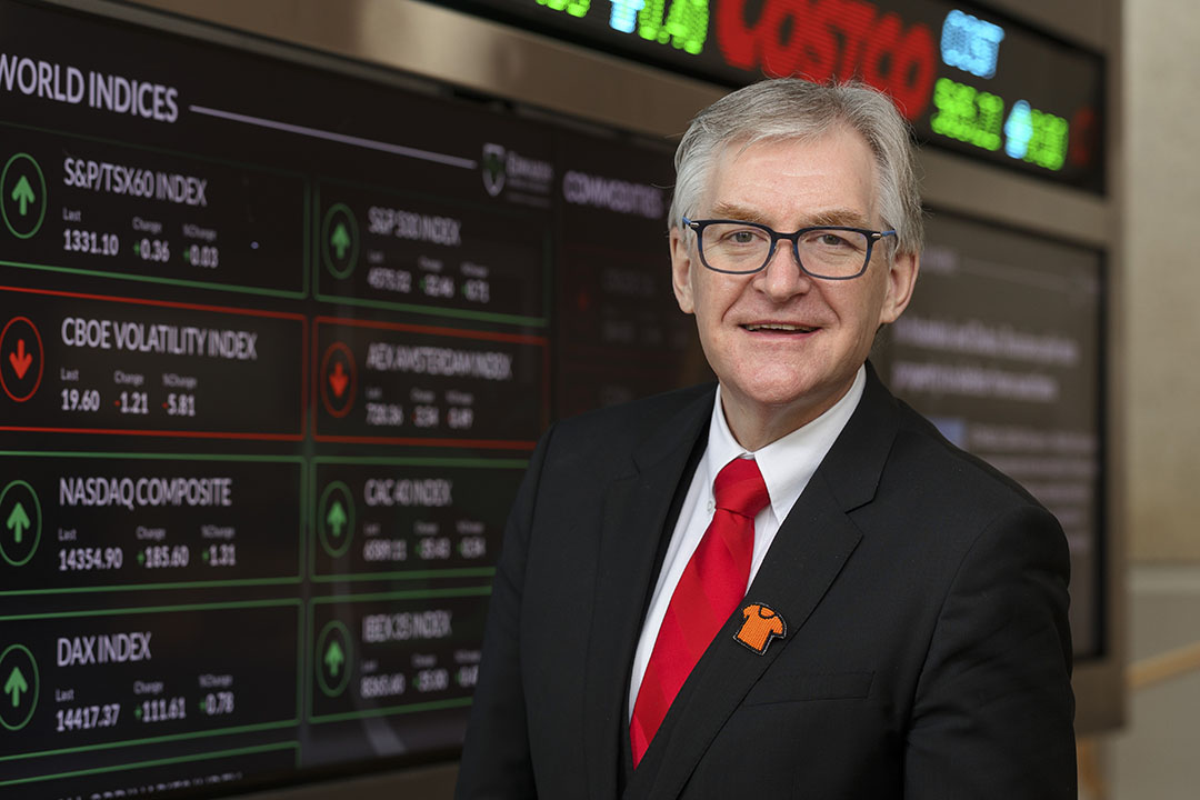 The dean of the Edwards School of Business, Dr. Keith Willoughby (PhD), in front of the N. Murray Edwards Market Watch stock ticker. (Photo: David Stobbe)