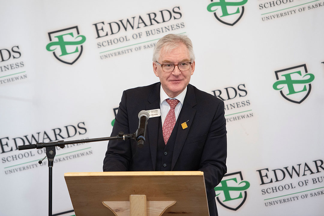 The dean of the Edwards School of Business, Dr. Keith Willoughby (PhD), in front of the N. Murray Edwards Market Watch stock ticker. (Photo: David Stobbe)