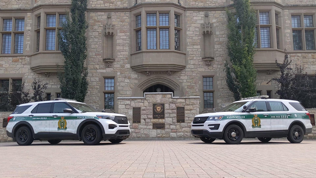 Two campus protective service vehicles are parked in front of a historic brick building