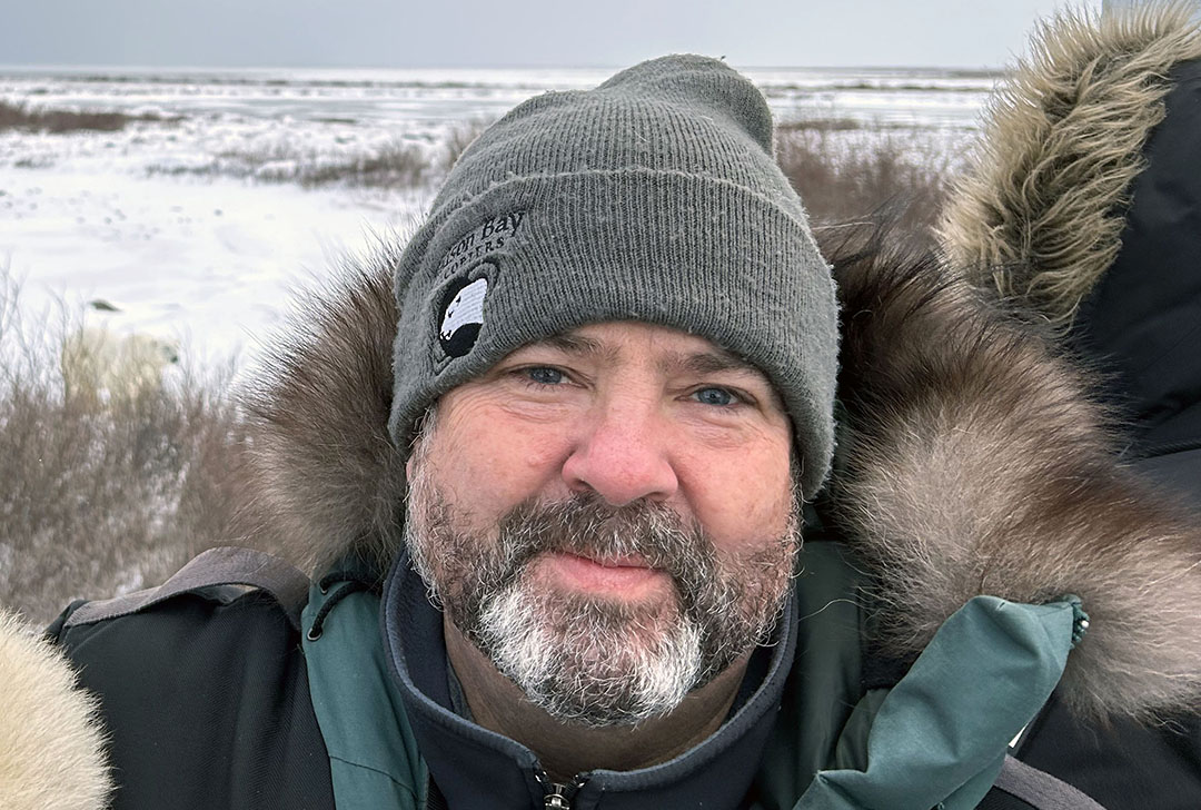 A man poses in a touque and a parka in a winter setting