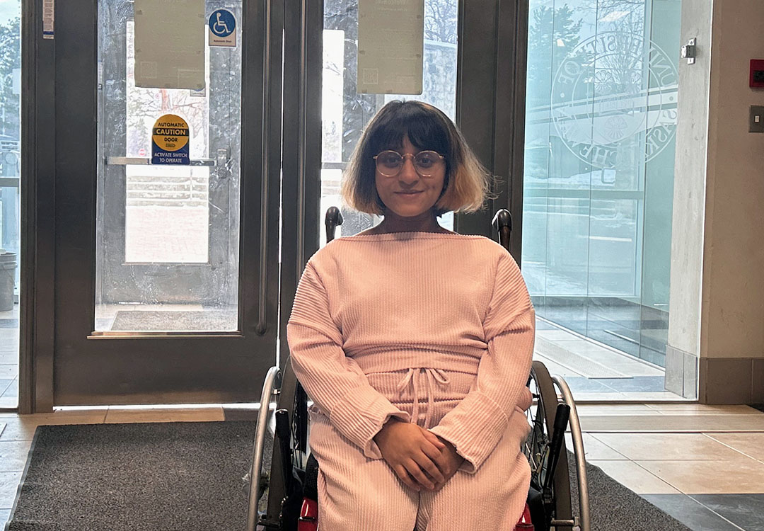 A person in a wheelchair poses in front of a set of doors